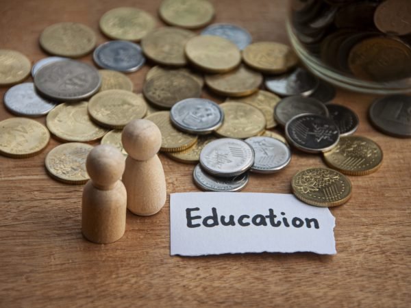 Education text on torn paper with jar, coins, wooden dolls and wooden table background. Education and savings concept
